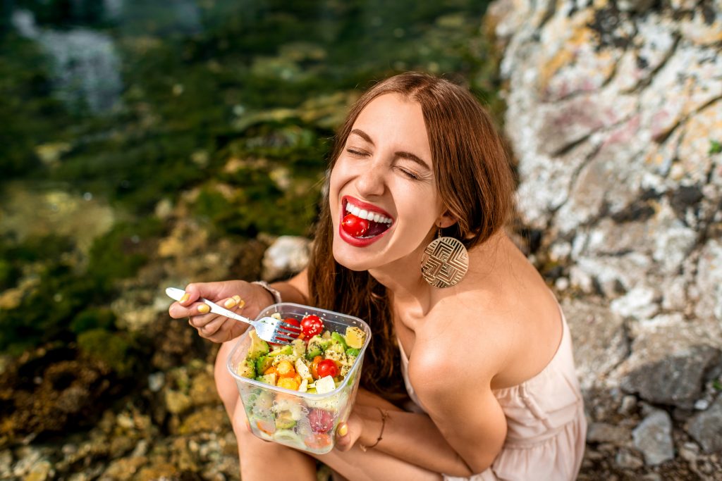 Woman eating healthy salad from plastic container near the river