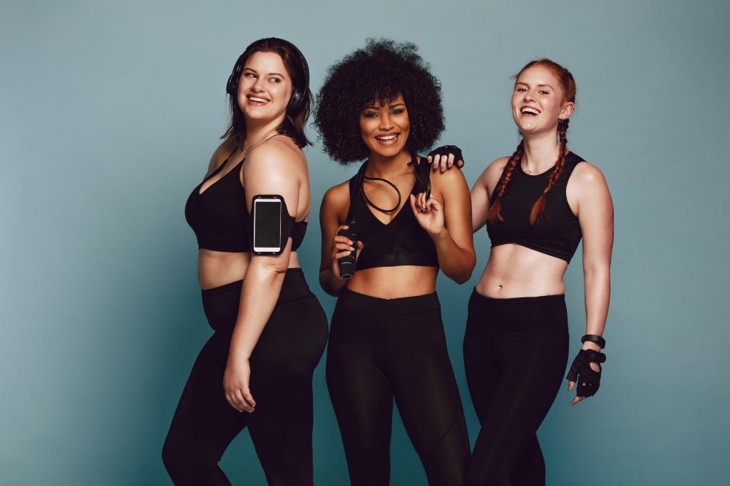 Portrait of mixed race women standing together against grey background and laughing. Diverse group women in sportswear.